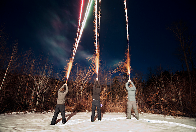 picture of three boys shooting mortar-type fireworks into the night sky