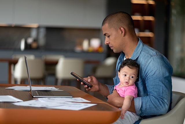 Un hombre sostiene a un bebe mientras mira un telefono.