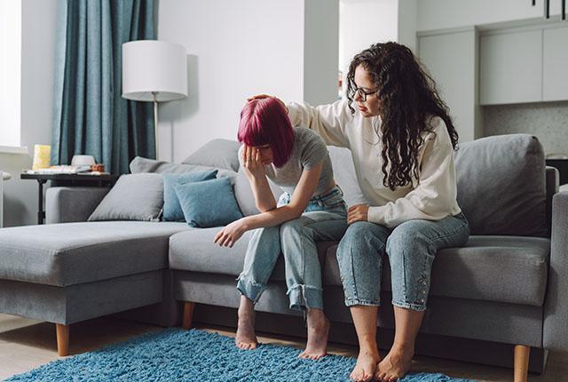 A woman comforts a teen girl while sitting on a couch.