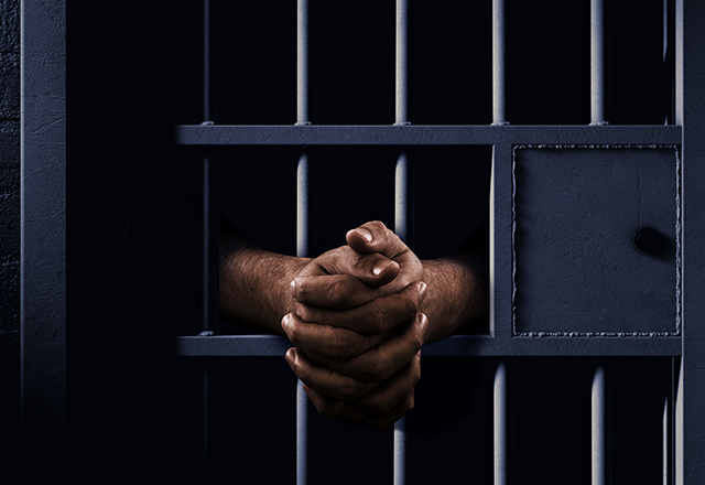 picture of a man's hands showing between cellblock bars in an African prison