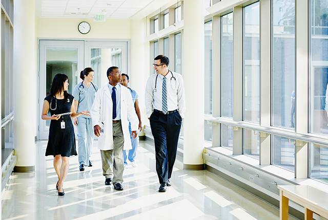 picture of several clinicians walking in close proximity in a sunny hospital corridor