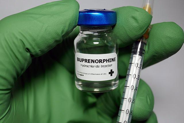 Vial of injectable buprenorphine held in gloved hand and a needle for injecting